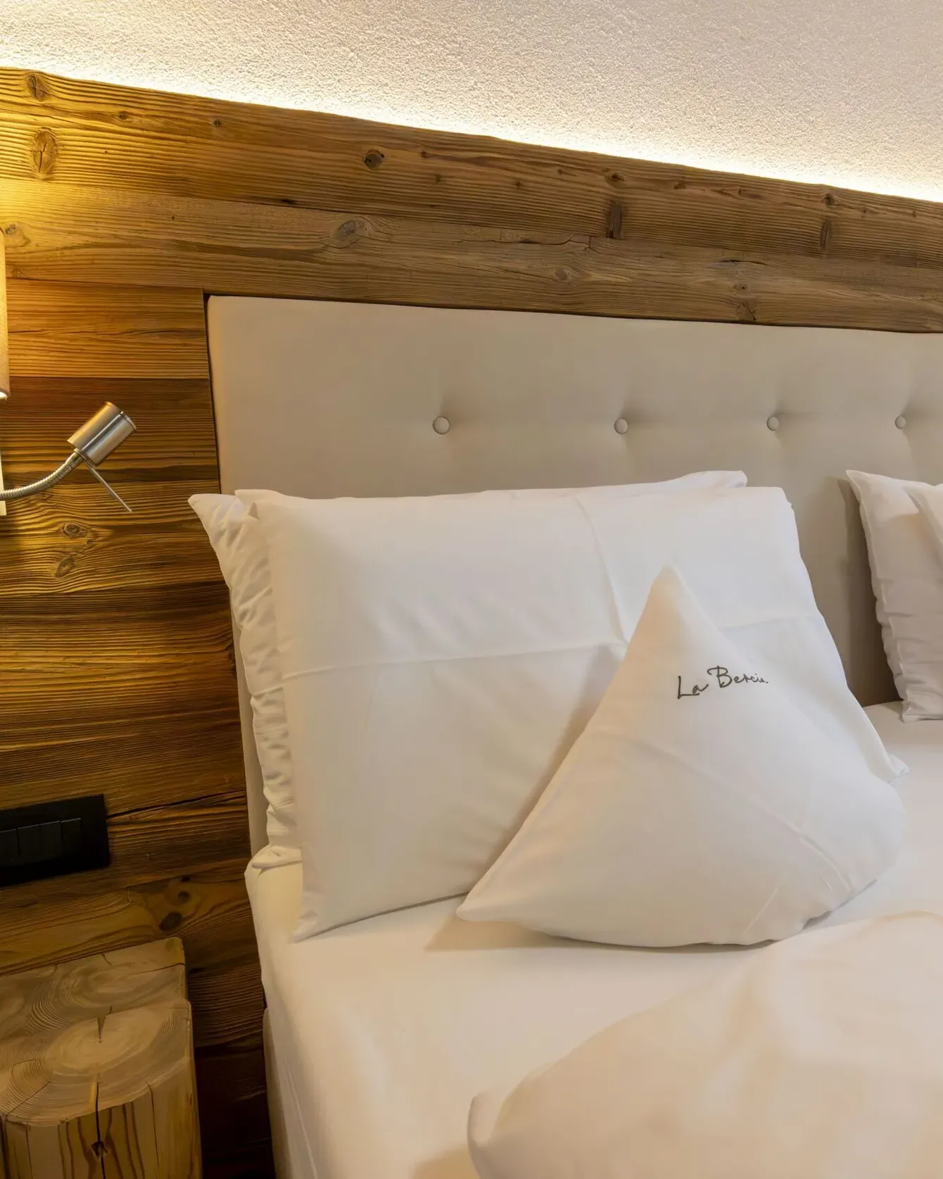 Luxurious hotel bedroom with a wooden paneled wall, tufted beige headboard, and white pillows.