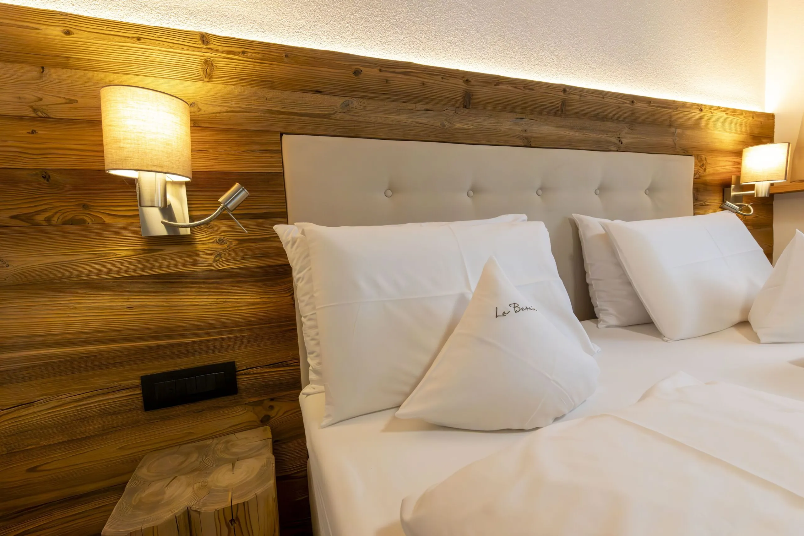 Luxurious hotel bedroom with a wooden paneled wall, tufted beige headboard, and white pillows.