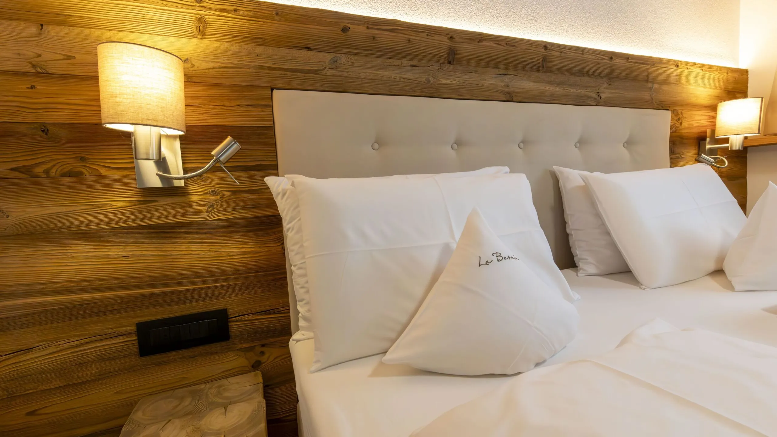 Luxurious hotel bedroom with a wooden paneled wall, tufted beige headboard, and white pillows.