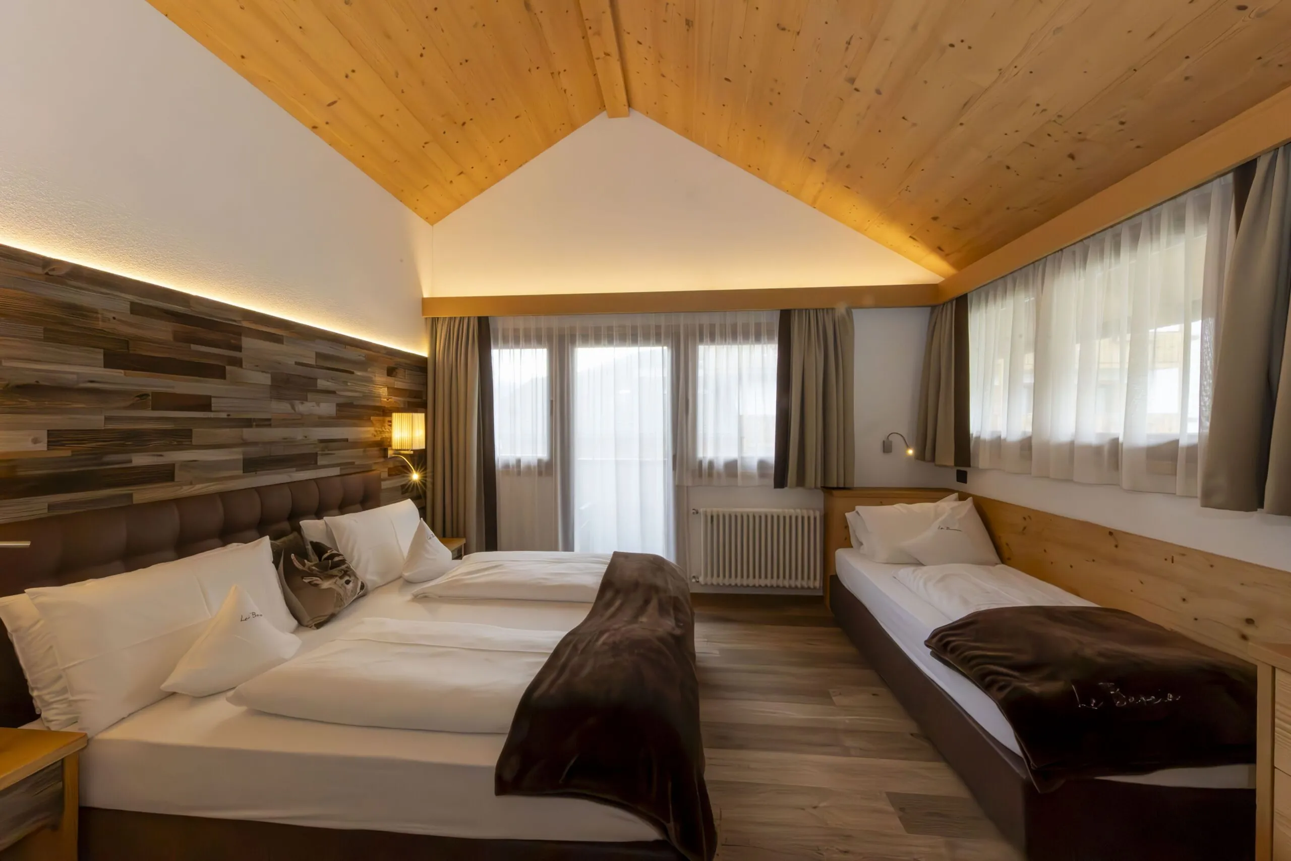 Cozy hotel room with a large bed and a smaller twin bed, wooden ceiling, and warm lighting.