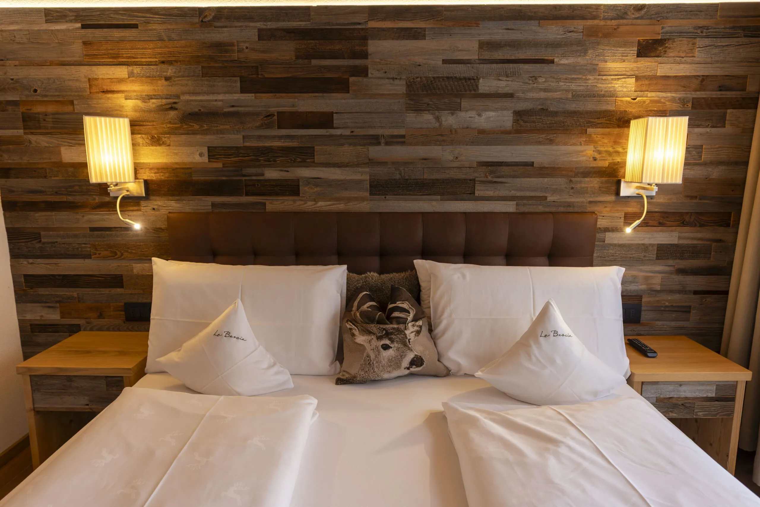 Wood-paneled headboard wall with two wall lamps, a plush bed, white pillows, and deer centerpiece.