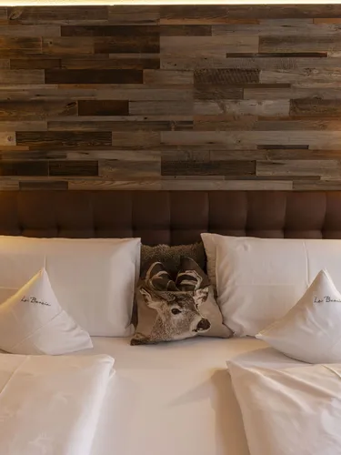Wood-paneled headboard wall with two wall lamps, a plush bed, white pillows, and deer centerpiece.