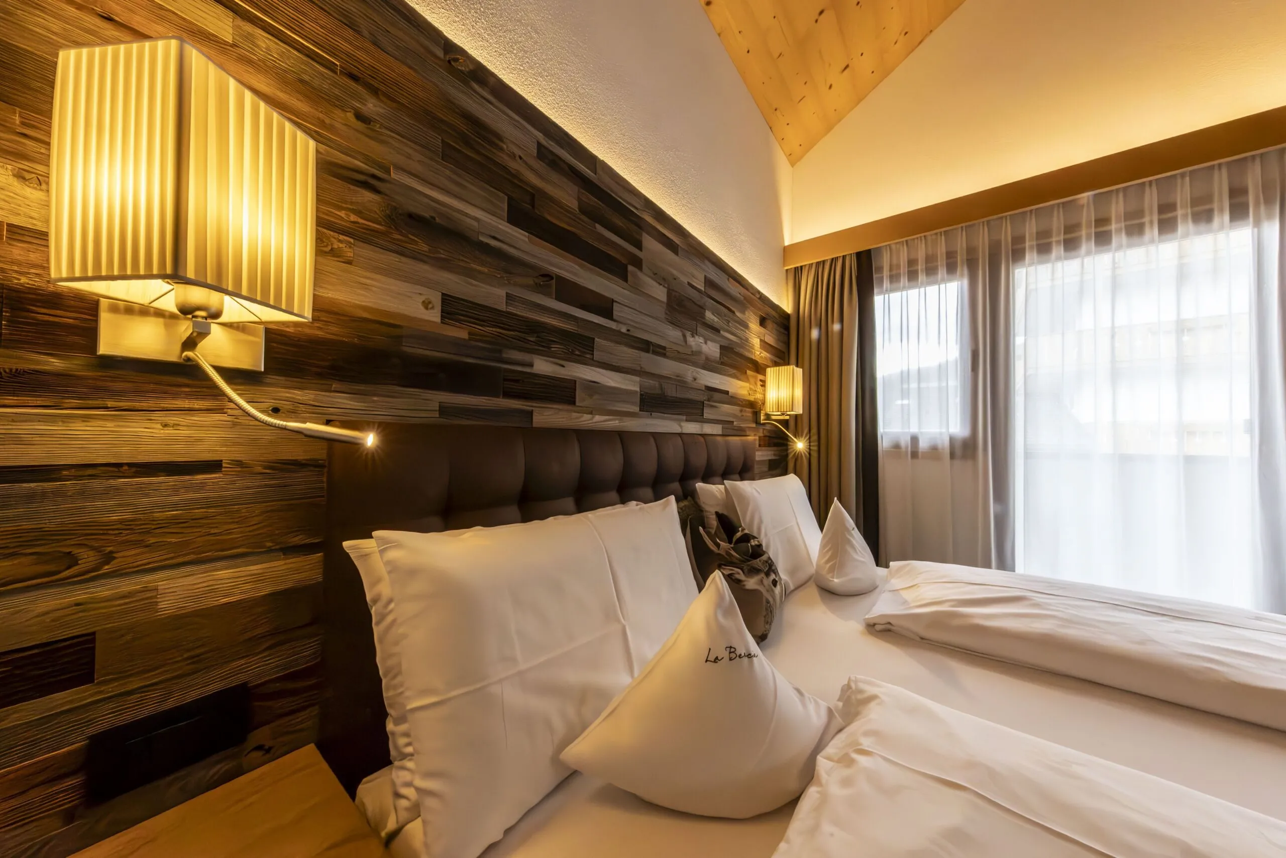 Cozy hotel bedroom with a wood paneled accent wall, twin beds, and warm wall lamps.