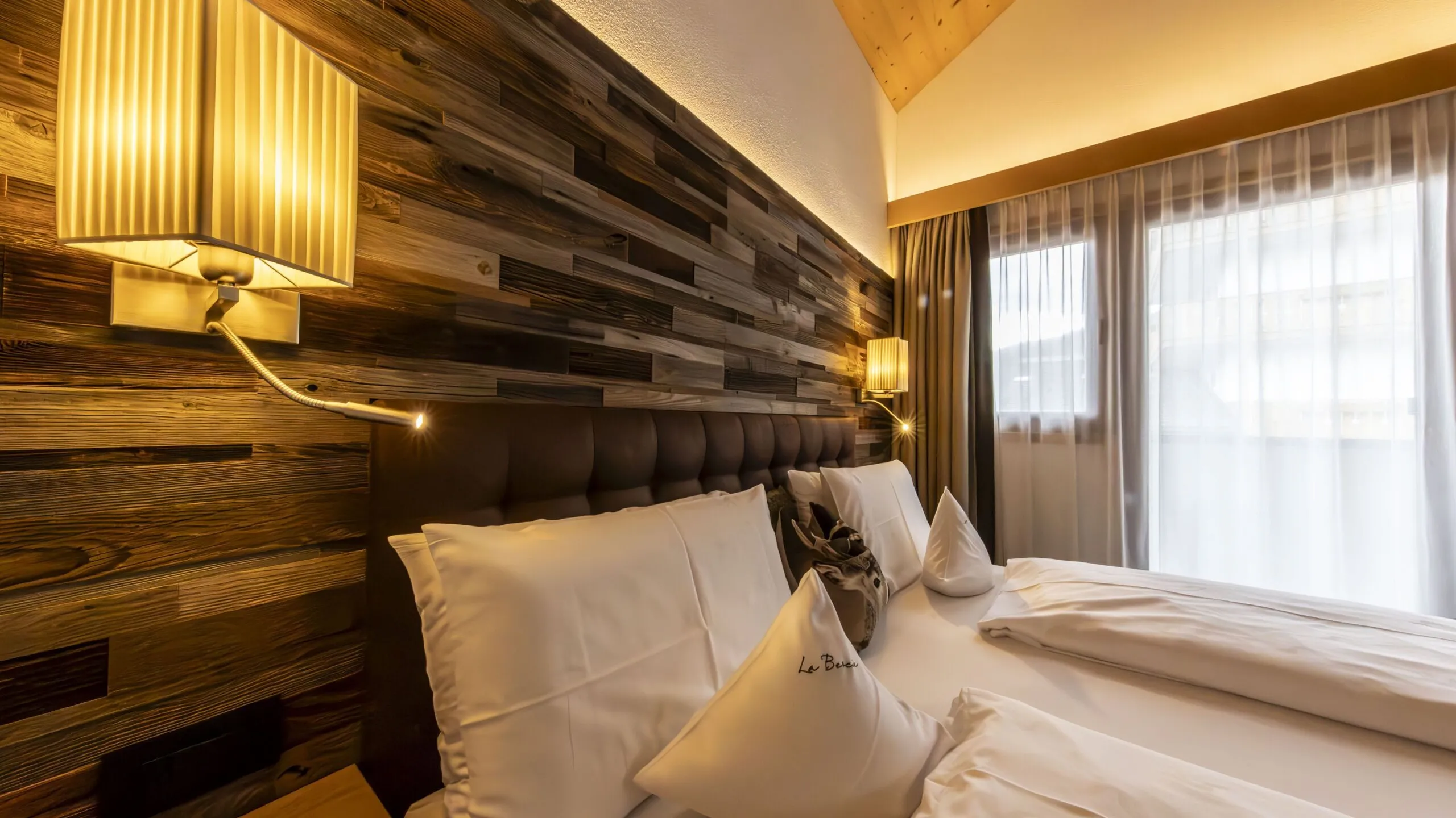 Cozy hotel bedroom with a wood paneled accent wall, twin beds, and warm wall lamps.