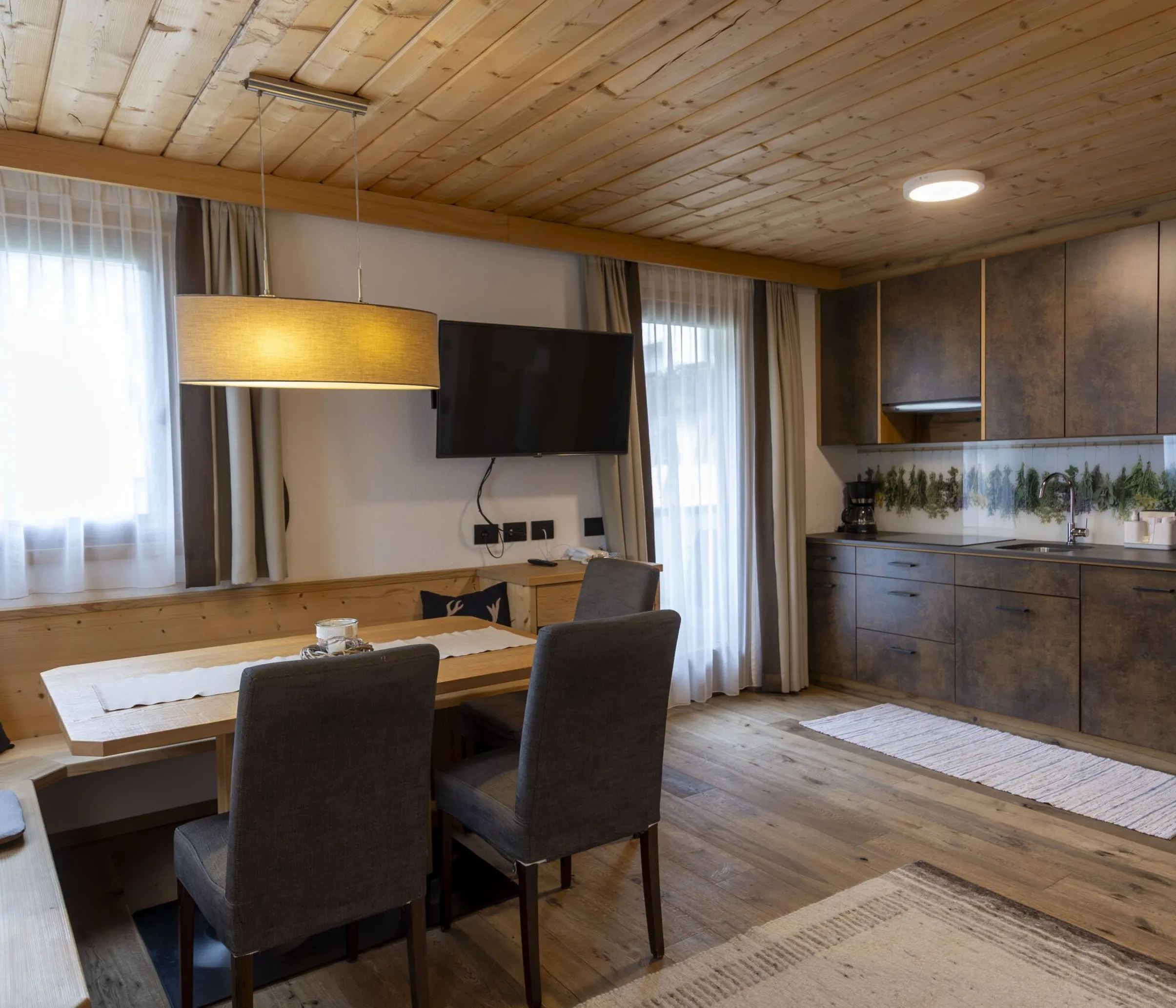 Cozy alpine dining area with wooden ceiling, solid wood table, gray chairs, and a wall-mounted TV.