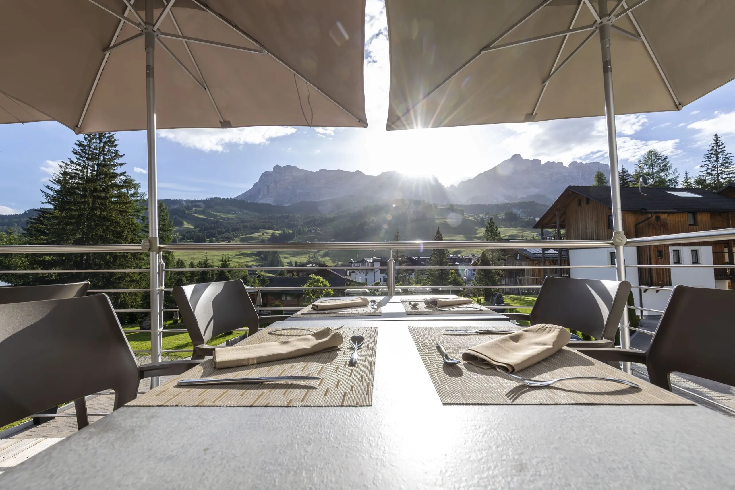 Al fresco mountain terrace with tables set for dining, sunlit valley and rugged peaks beyond.