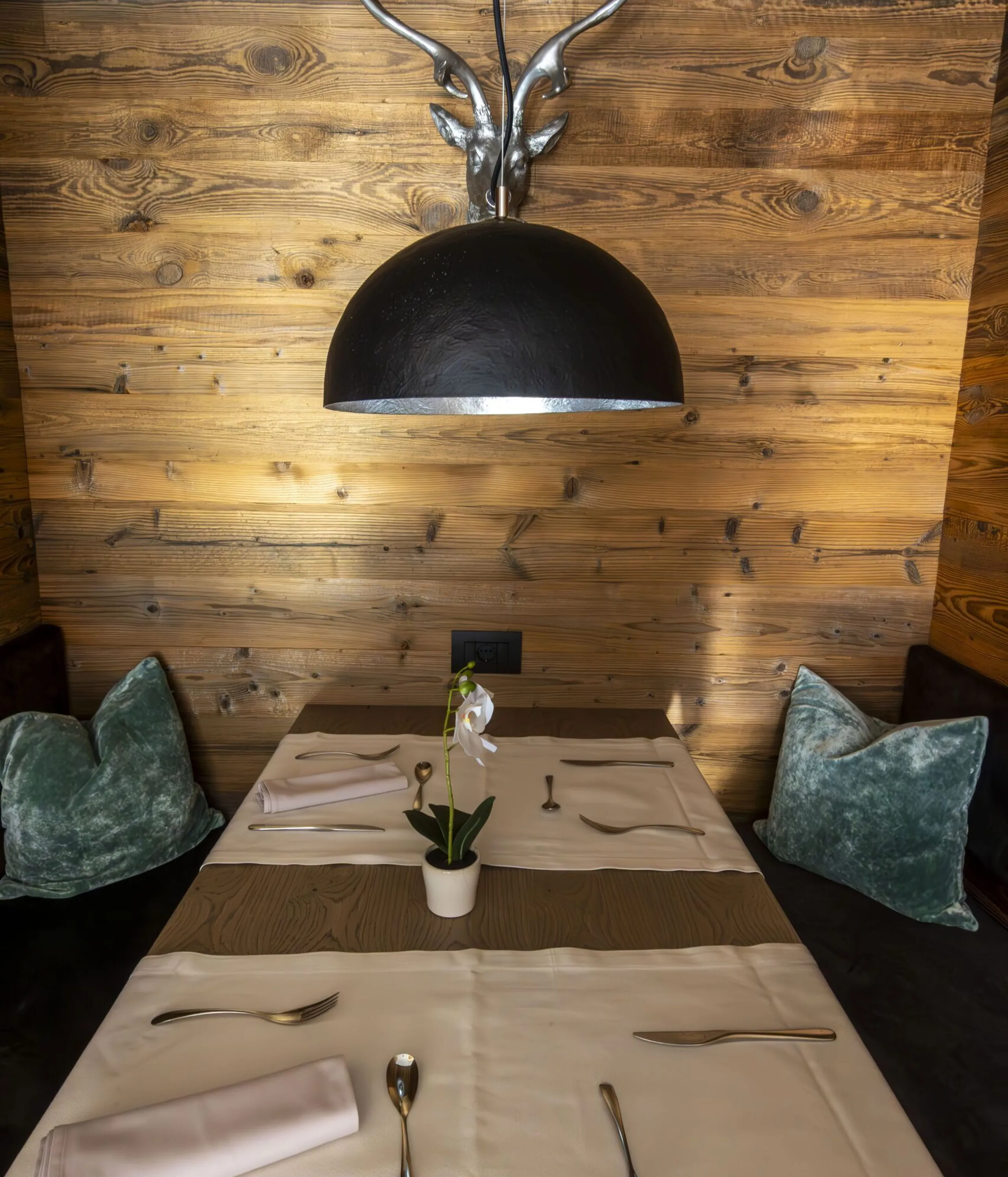 Cozy wooden dining nook with a black dome light and antler fixture over a table set with white linen and silverware