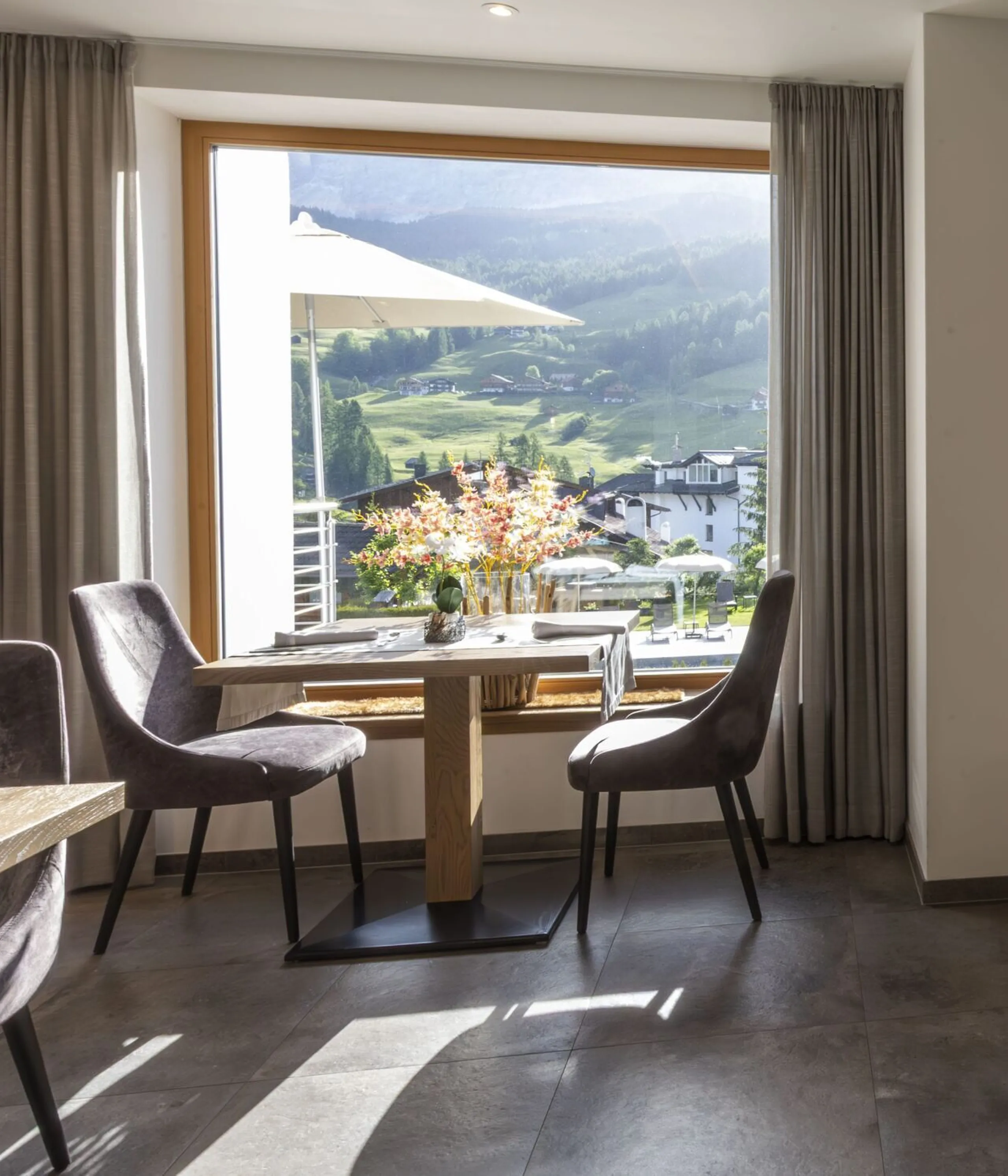 Cozy hillside restaurant with wooden ceilings, large window view of mountains, and dining tables with gray chairs.