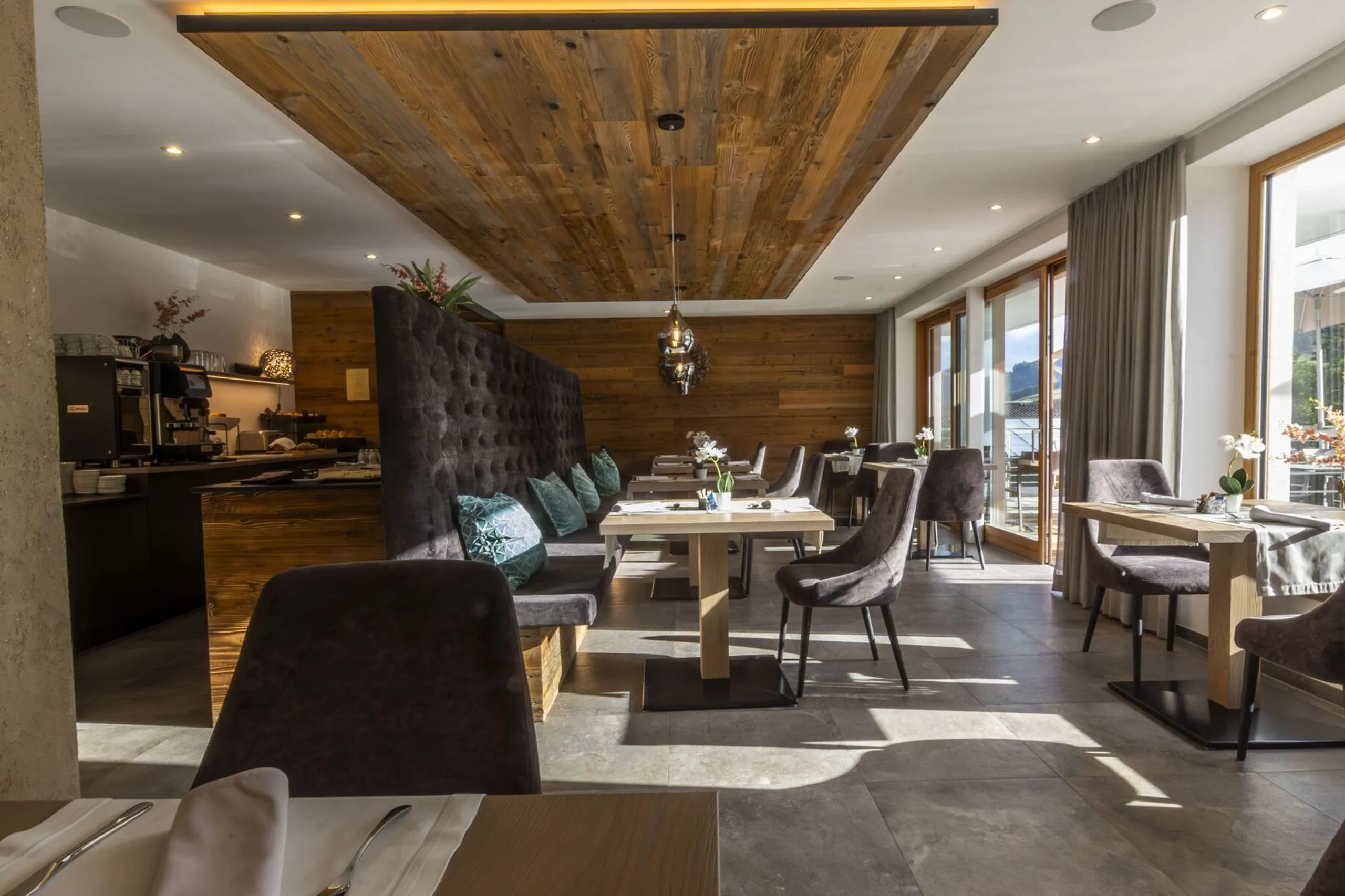 Cozy modern restaurant interior with wooden ceiling panel, plush seating, and large windows.