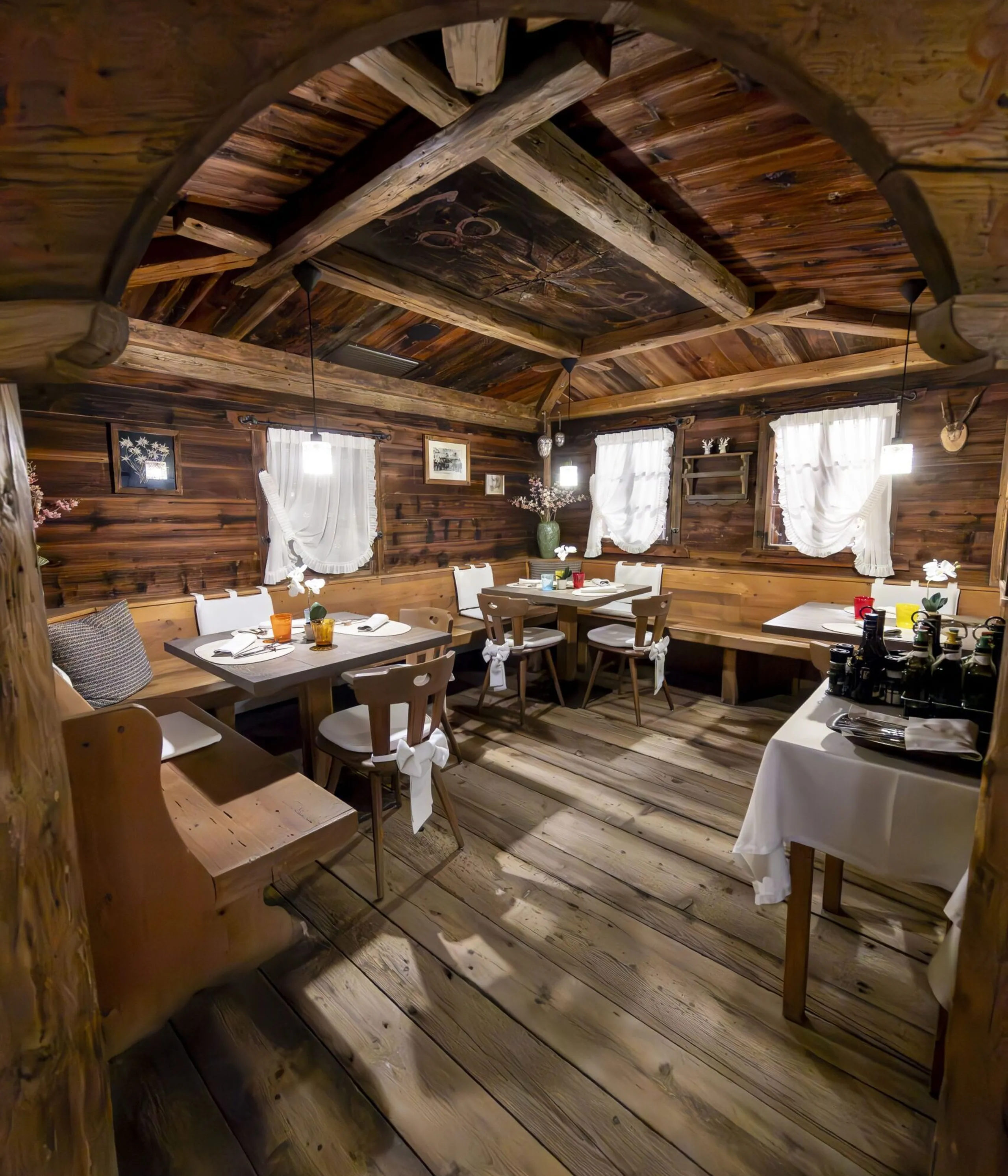 Cozy rustic dining room with wooden walls, arched ceiling, and tables set with white linens and chairs.