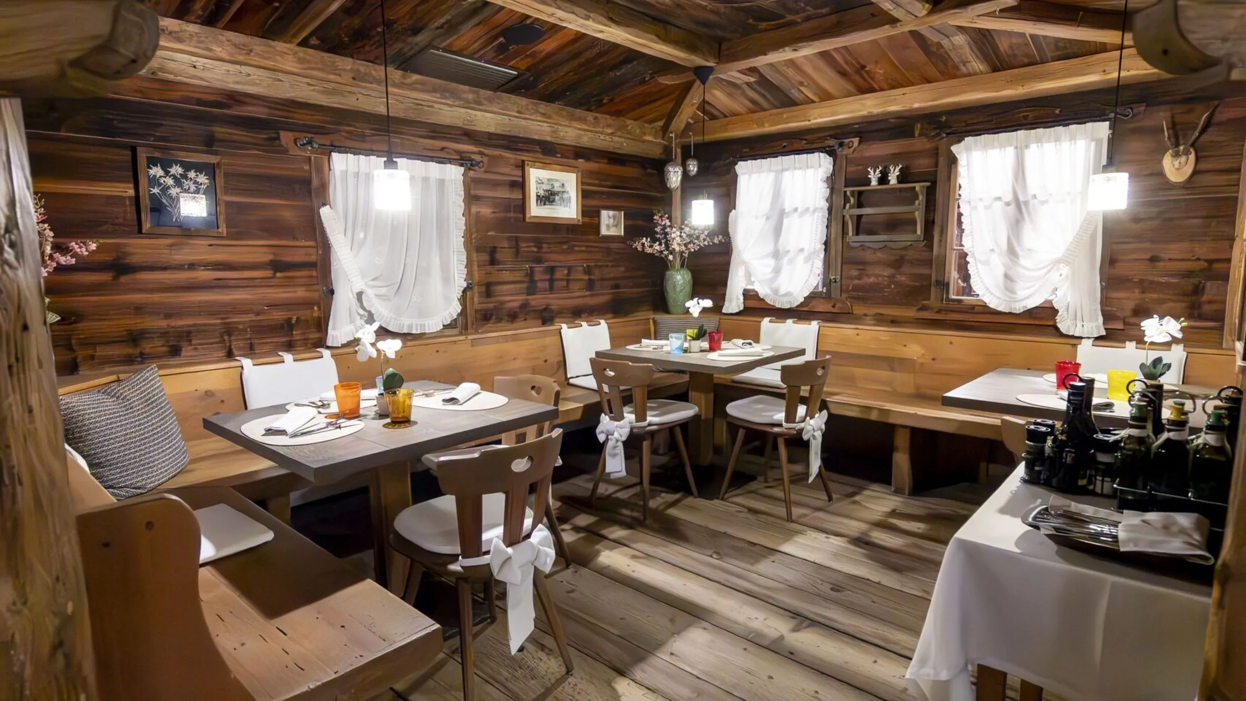 Cozy rustic dining room with wooden walls, arched ceiling, and tables set with white linens and chairs.