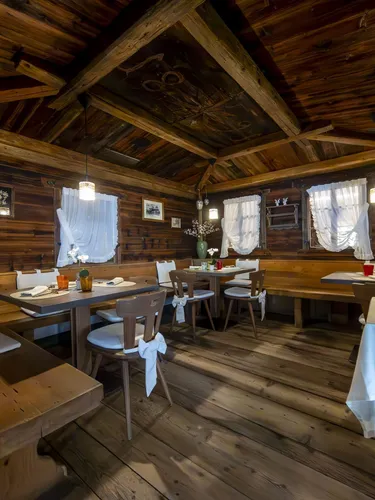 Cozy rustic dining room with wooden walls, benches, tables set for meals, white curtains, and warm lighting.