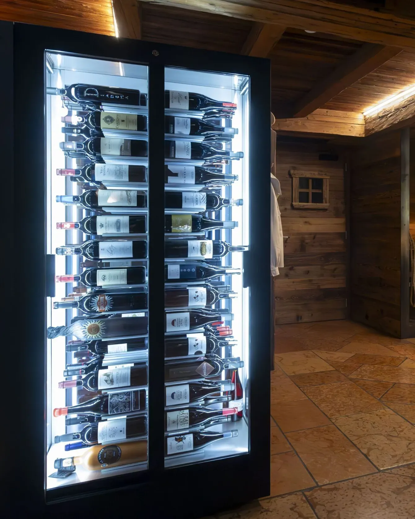 Luxurious wine fridge with illuminated bottles beside a rustic wood bar in a warmly lit interior