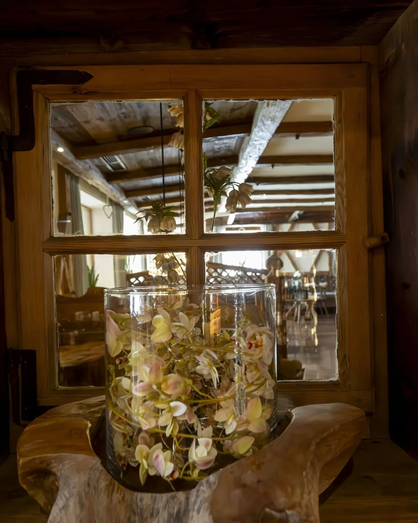 A wooden windowsill vignette with a glass jar of pastel dried flowers inside a rustic interior.