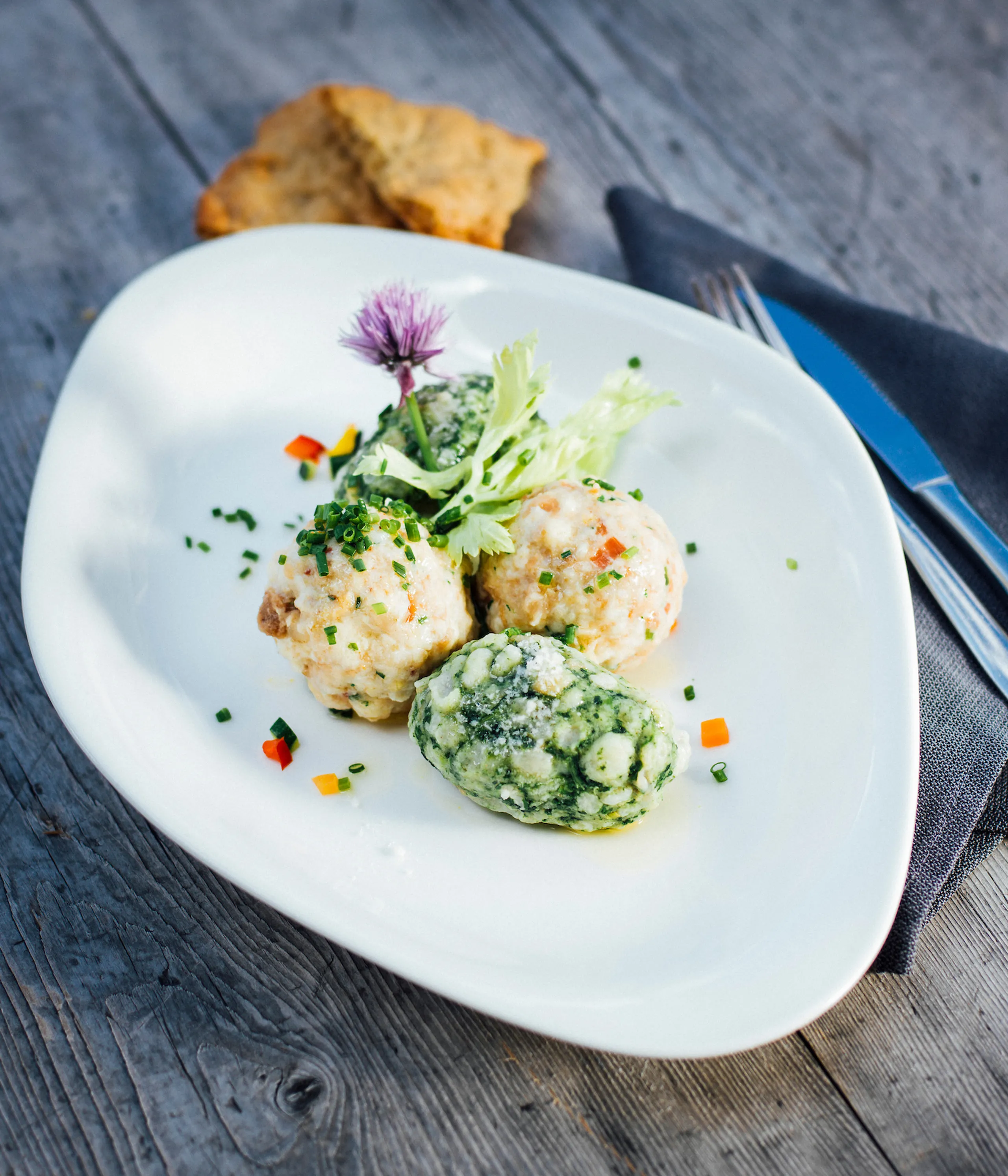 Three herb-speckled dumplings on a white plate with greens, carrot bits, and a purple flower garnish