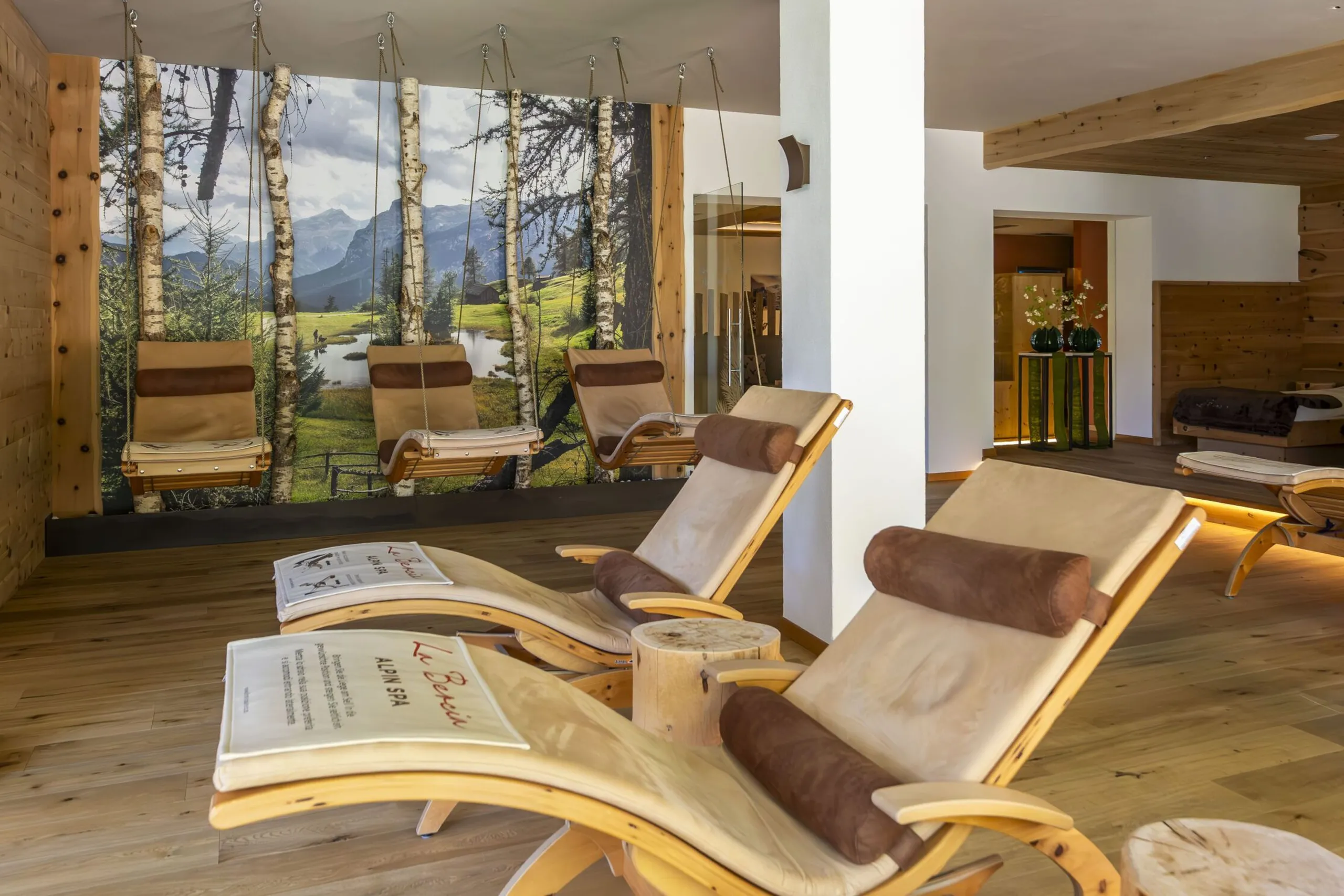 Cozy spa lounge with wood furniture, hanging chairs, and a forest mural backdrop in a sunny wellness space