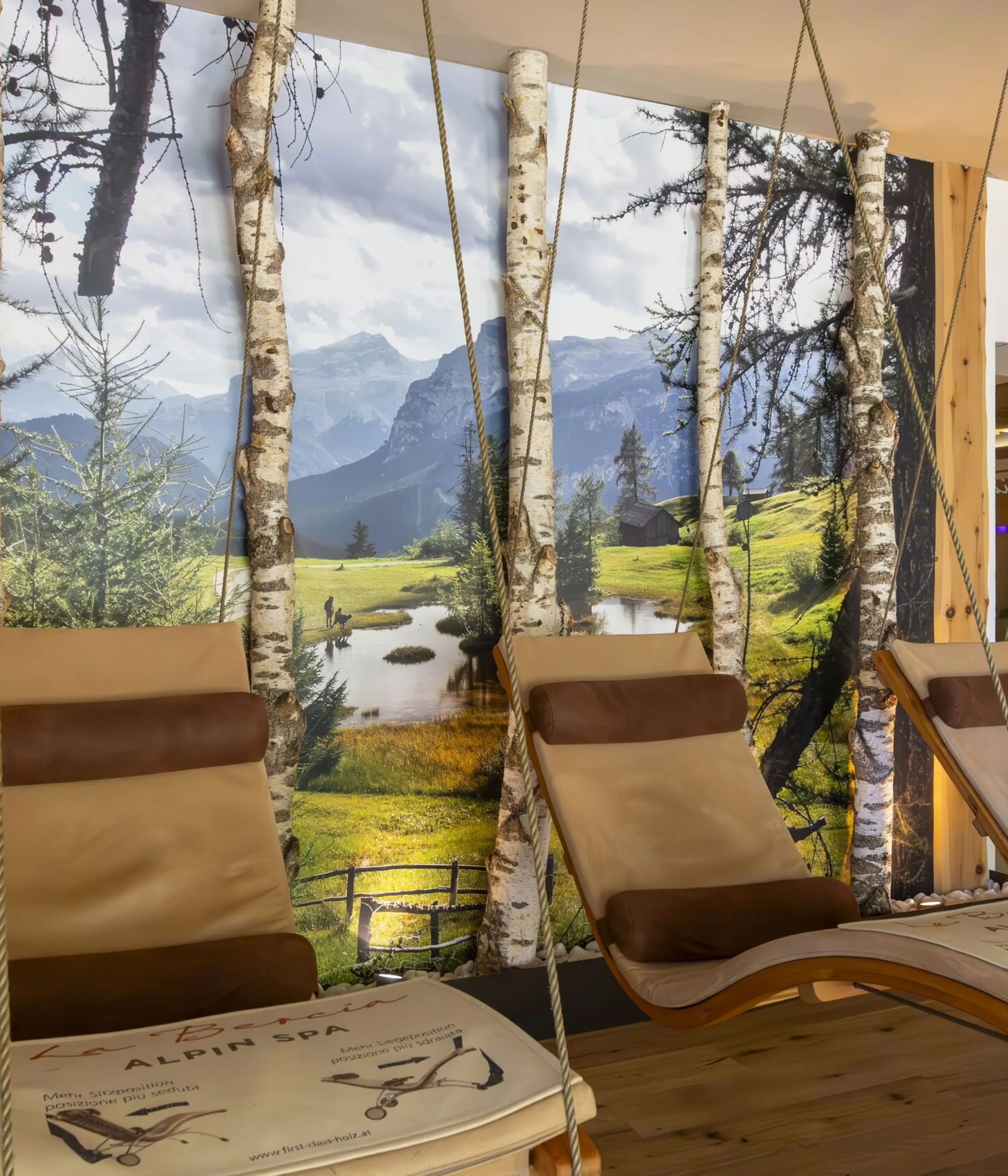 Relaxing hanging lounge chairs in a wooden spa area with a mountain meadow mural backdrop.