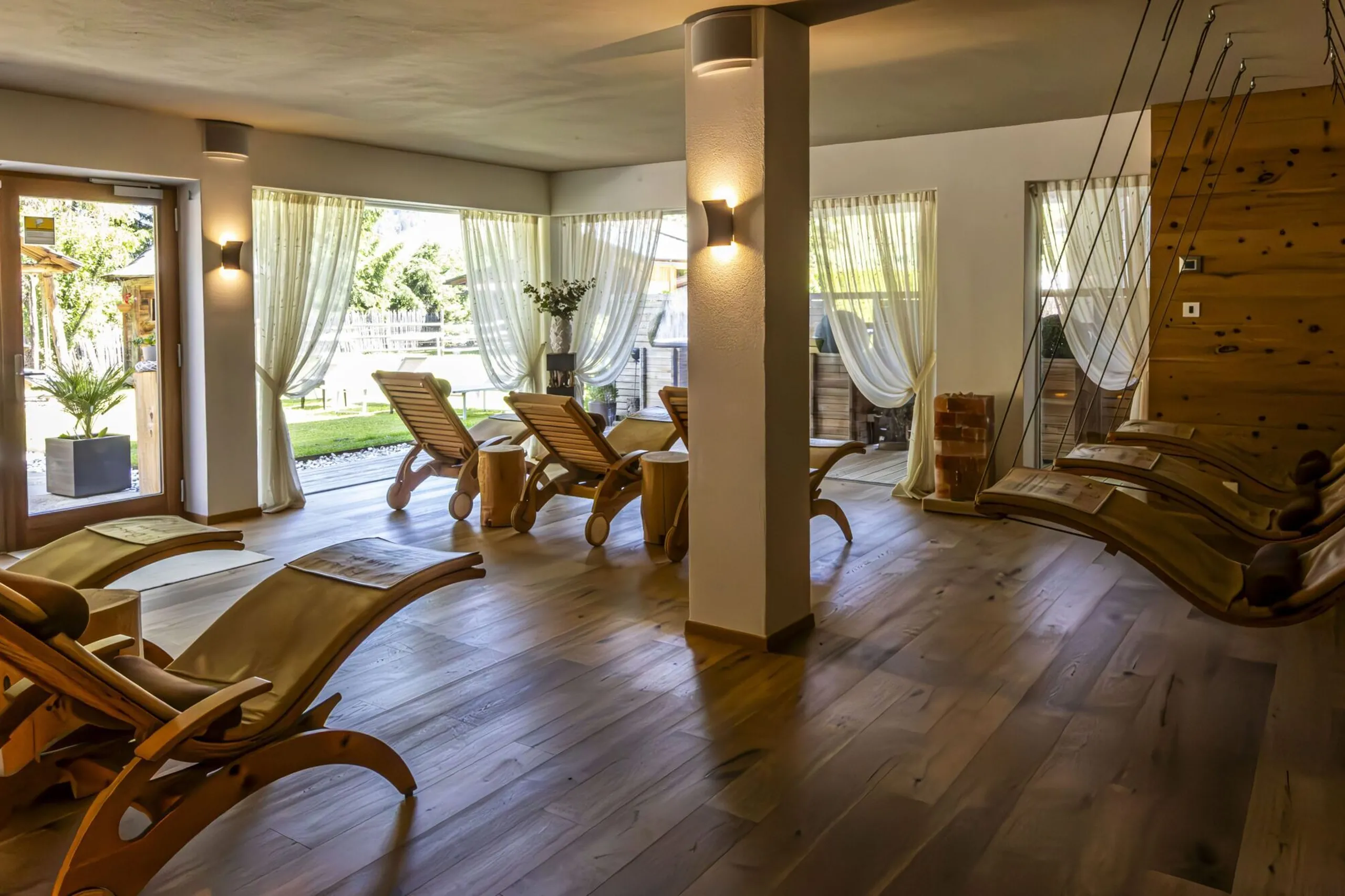 Relaxing indoor spa with wooden lounge chairs, soft curtains, and a sunny outdoor view.