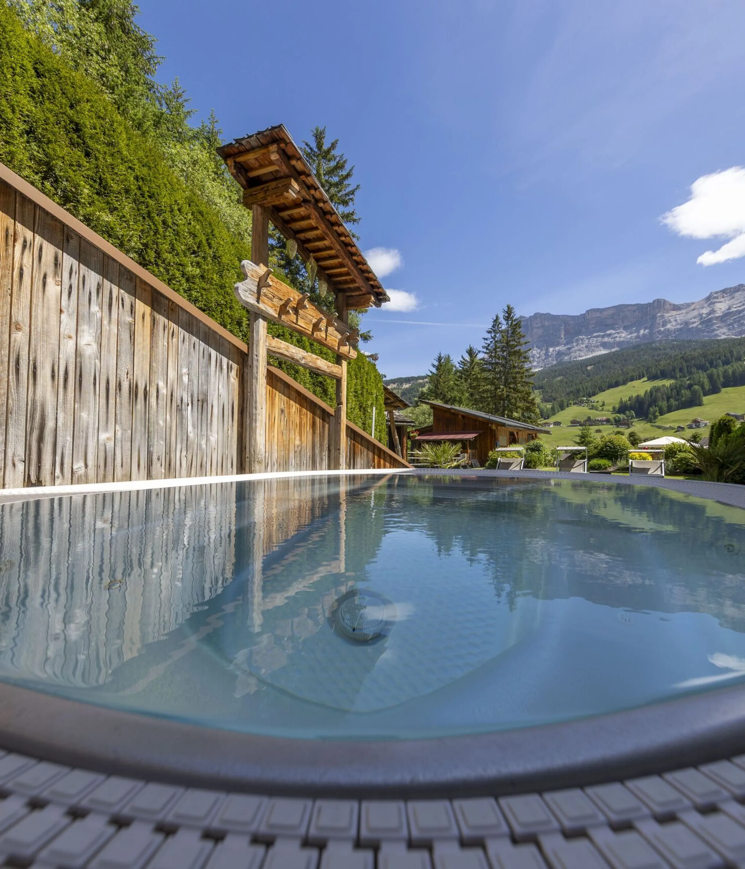 Outdoor hot tub with glassy water, wooden fence, and alpine mountains in the background.