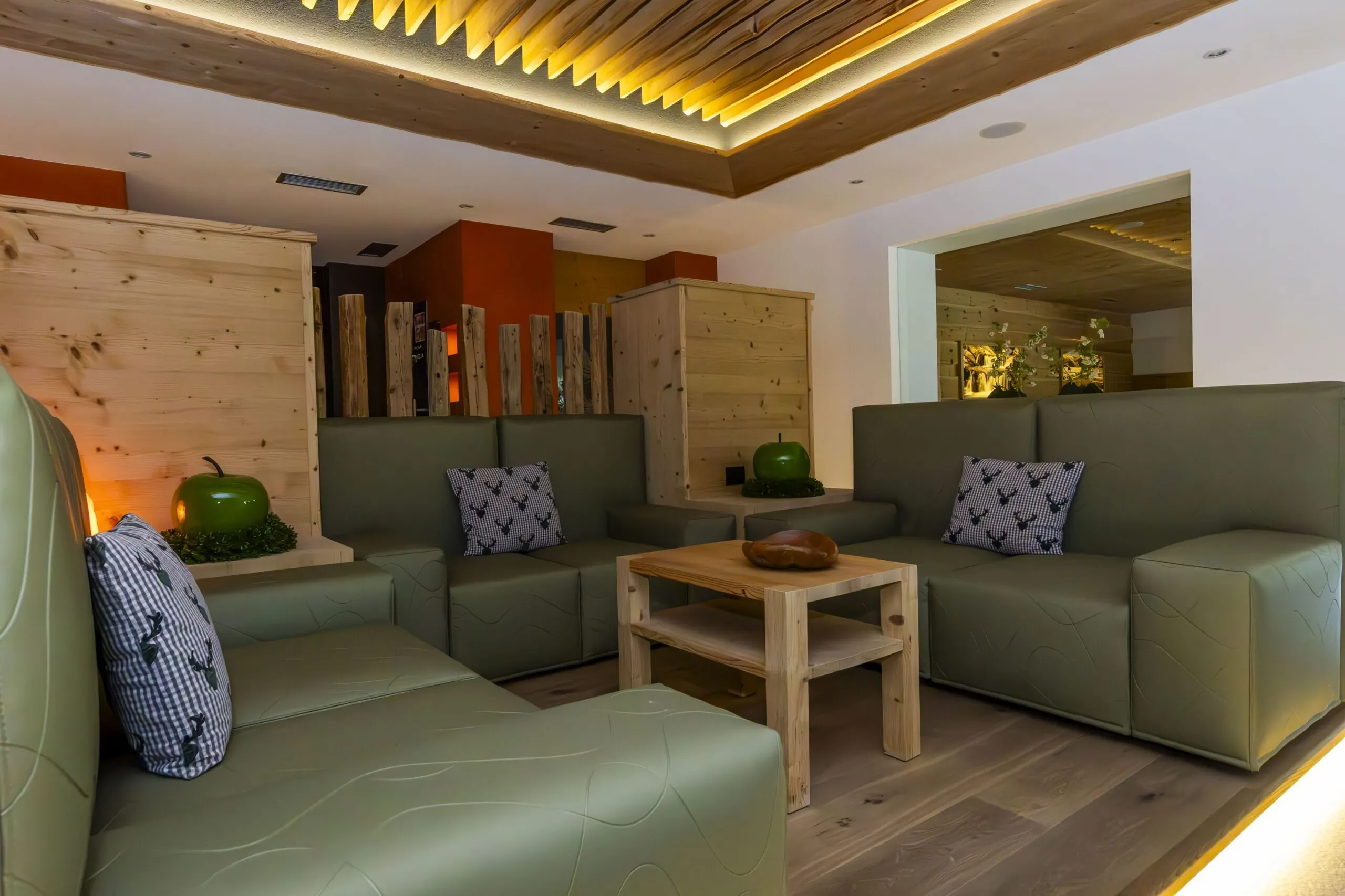 Cozy lobby with green modular seating, wooden coffee table, decorative pumpkins, and warm lighting.